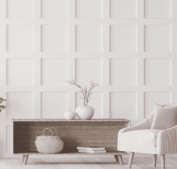 A minimal living room with a wooden console table, two vases, a basket, an armchair, and a white grid paneled wall in the background.