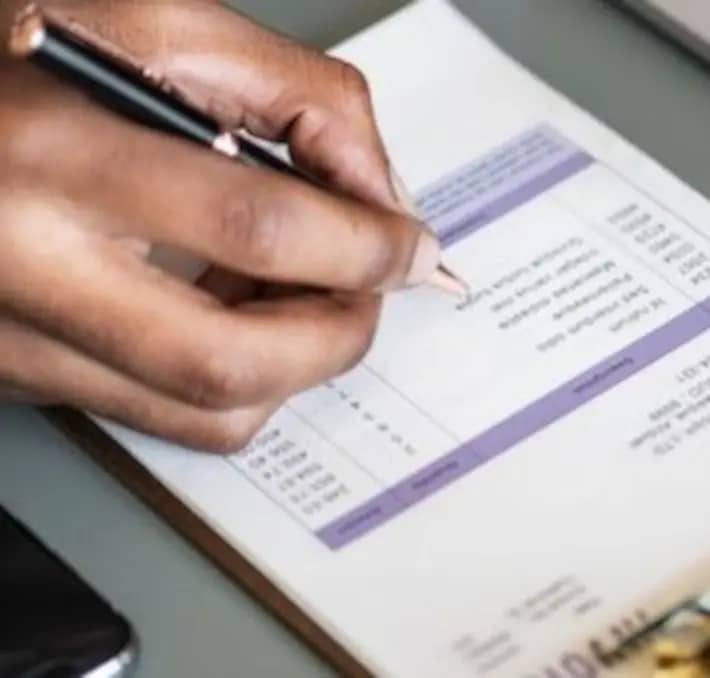 Close-up of a person’s hand holding a pen and filling out a form on a clipboard.