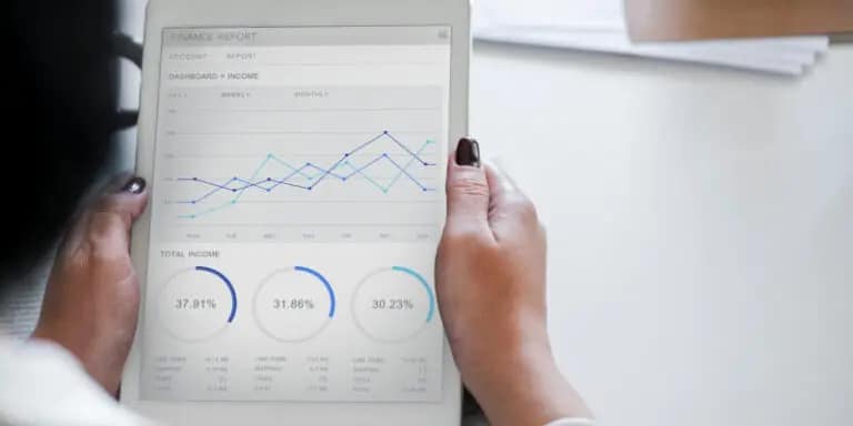 Person holding a tablet displaying a financial dashboard with a line graph and three circular charts showing percentages.
