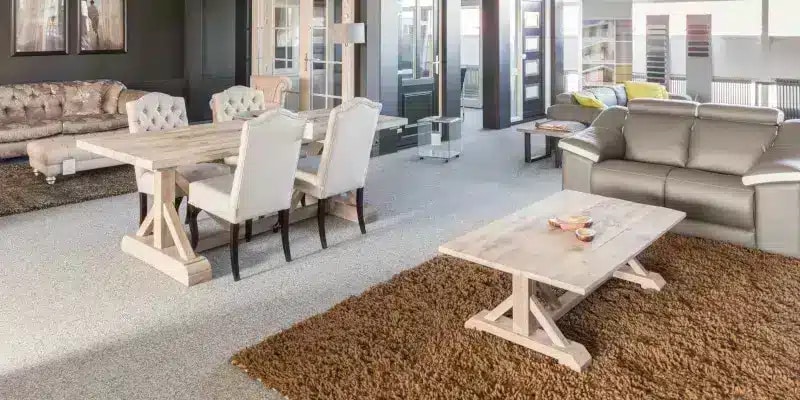 Spacious living and dining area with light wood furniture, beige chairs, gray sofa, shaggy brown rugs, and large windows letting in natural light.