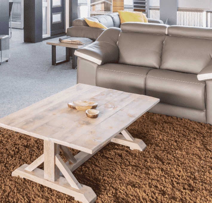 A modern living room with a gray sofa, a wooden coffee table holding small bowls, and a brown shaggy rug on the floor.