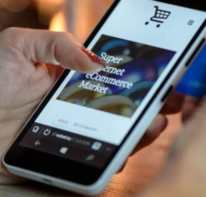 A person holds a smartphone displaying an eCommerce website with a shopping cart icon, while holding a credit card in the other hand.