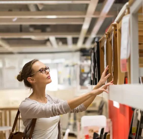 A woman wearing glasses browses and selects items from a display of wall-mounted folders in a store.