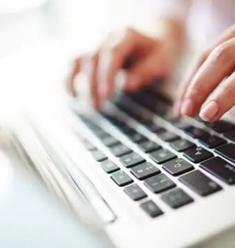 Close-up of hands typing on a laptop keyboard.