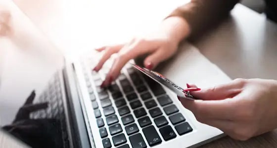 A person uses a laptop keyboard with one hand while holding a credit card in the other, suggesting online shopping or payment.