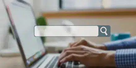 Person typing on a laptop keyboard with a search bar graphic overlayed in the foreground.